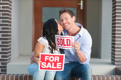 Happy couple holding for sale and sold signs kissing